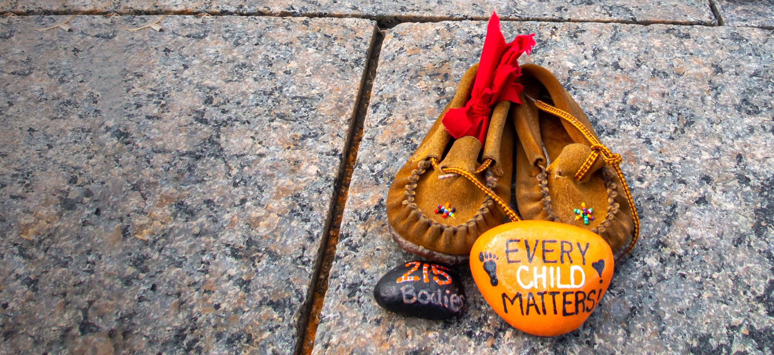 Children's shoes and a painted orange rock that reads "Every Child Matters" site at a memorial at Canada's Parliament Hill for Indigenous children who were sent to residential schools