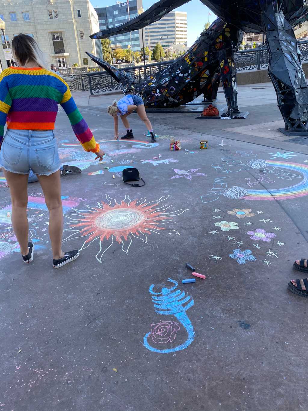 Milda pointing to a chalk sun surrounded by a scorpion, flowers, and a rainbow