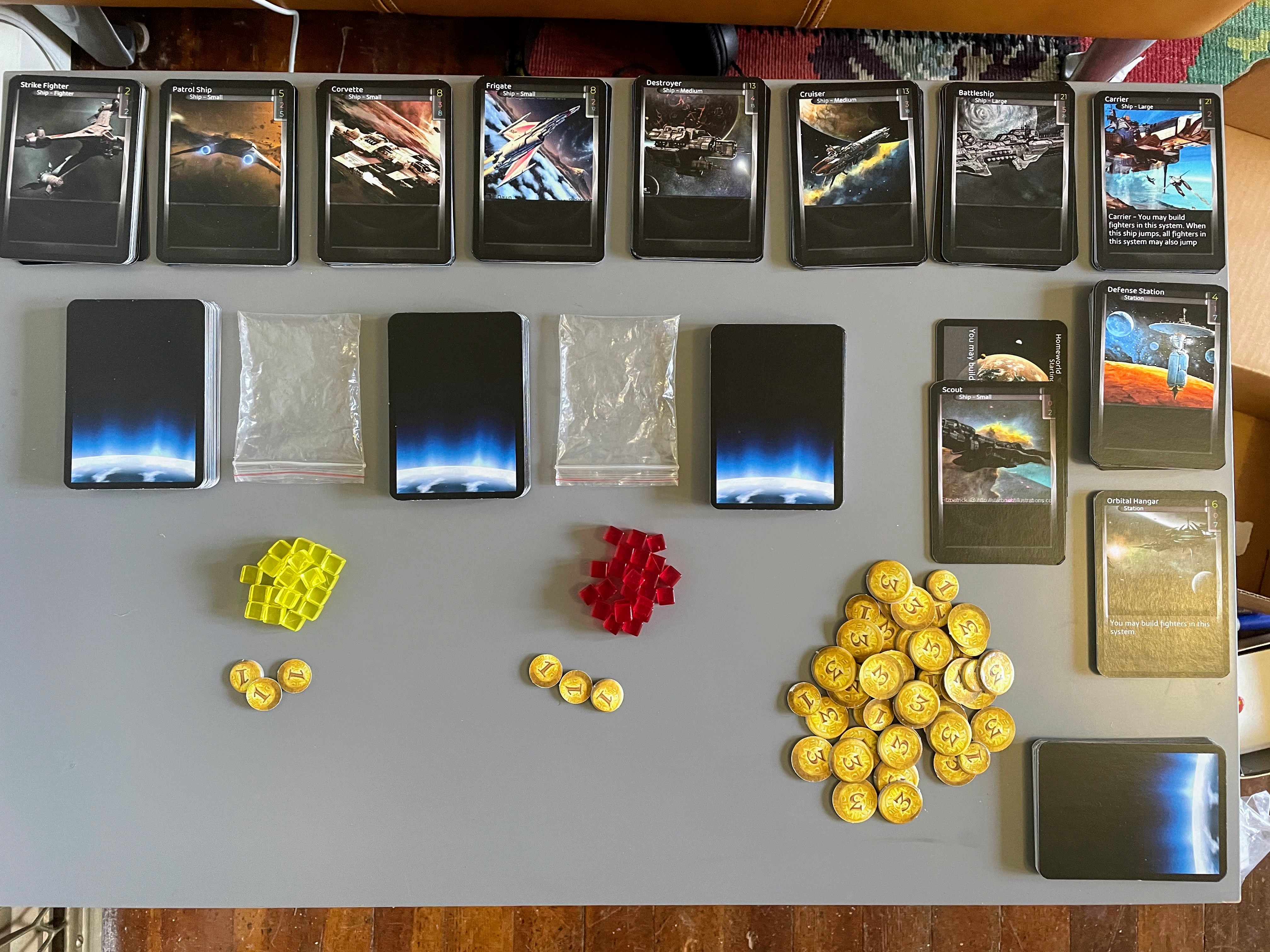 Stacks of cards are laid out on a table. Cards for ships are face up, with three decks set out face down. Tokens for developments and credits are also spread out.