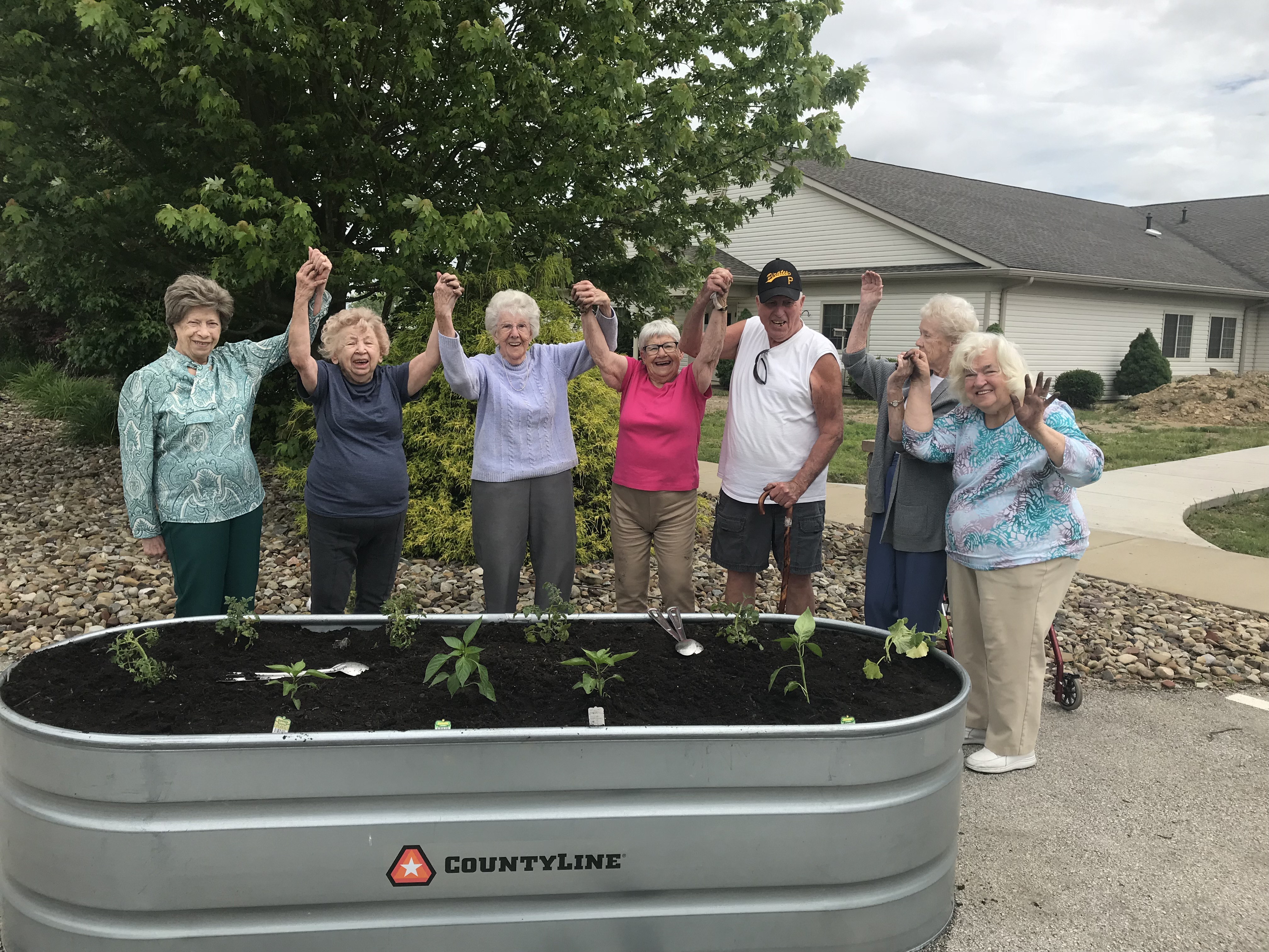 A group of residents at CrossRoads raise their hands in celebration of their newly planted garden
