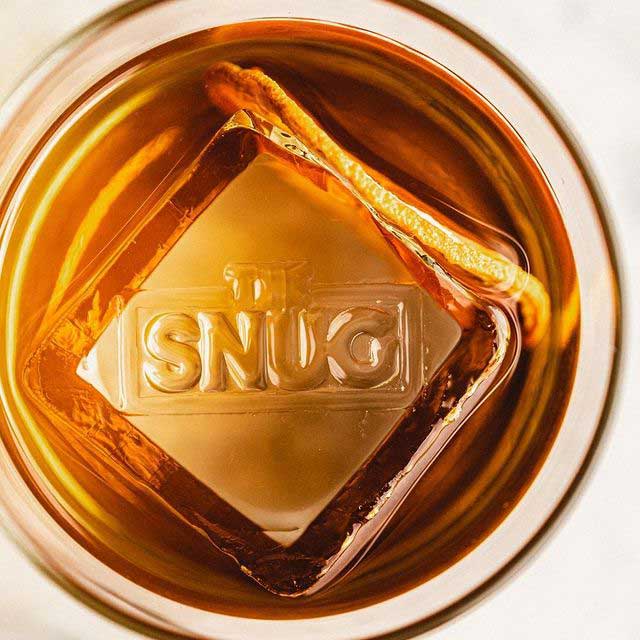 Image of an artisan ice cube stamped with The Snug logo.