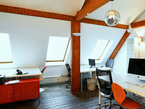 Contemporary loft style office workspace featuring prominent wooden beams over wooden computer desks and black chairs Zoom background
