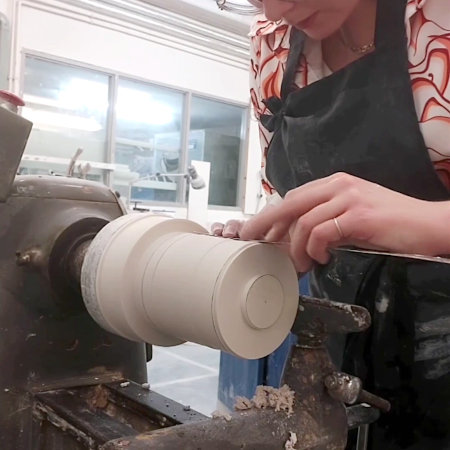 Francesca checking the measurements of a plain cylindrical cast of plaster, that has been marked up in pencil and mounted on a lathe.