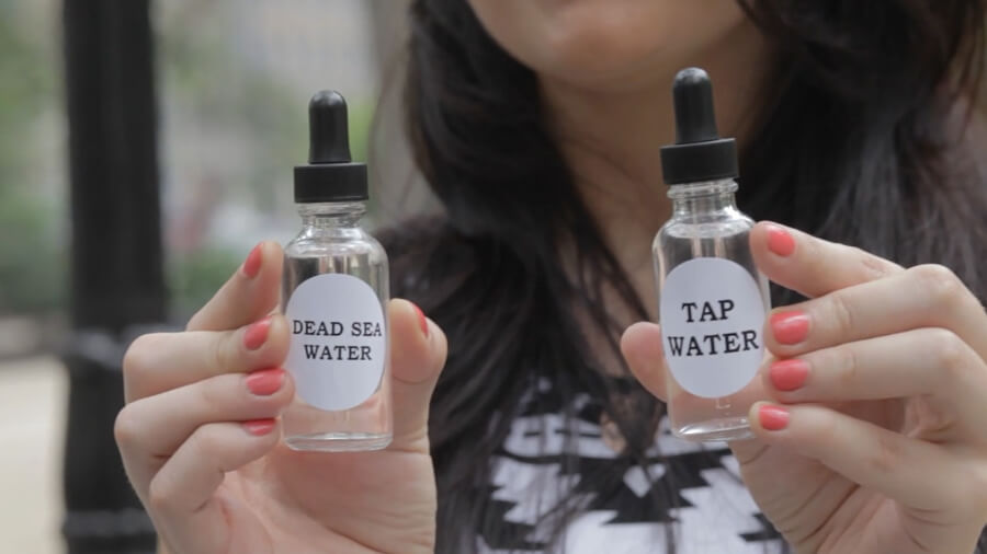 Woman holding bottles of Dead Sea water vs tap water.