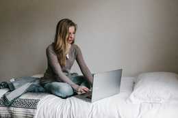 woman using her laptop while sitting on her bed