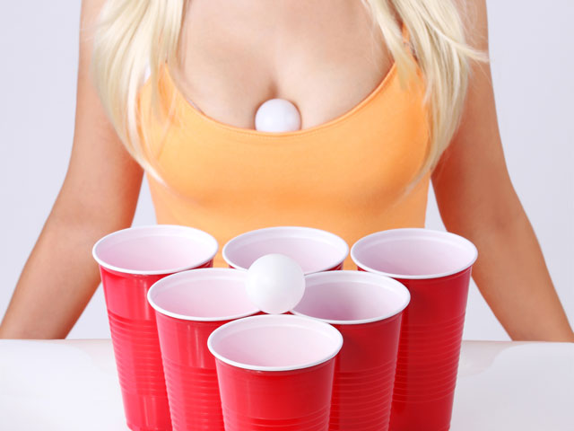 A female playing the Titties Drinking Game with a beer pong ball bouncing off her chest and into a plastic cup