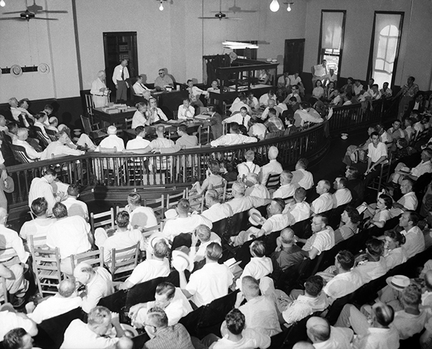 A black and white photo of a crowded 1950s courtroom shows the trial of Roy Bryant and J.W. Milam for the murder of Emmett Till.