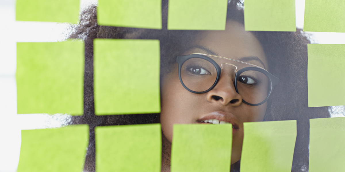 A UX designer peeking through a selection of Post-It notes A UX designer peeking through a glass wall, surrounded by Post-It notes