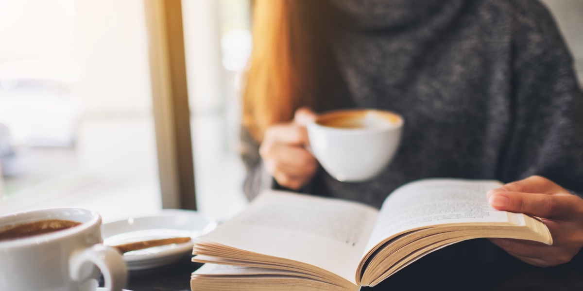 The Best Books for UX Writers Close up of someone in a grey sweater reading a book and drinking coffee