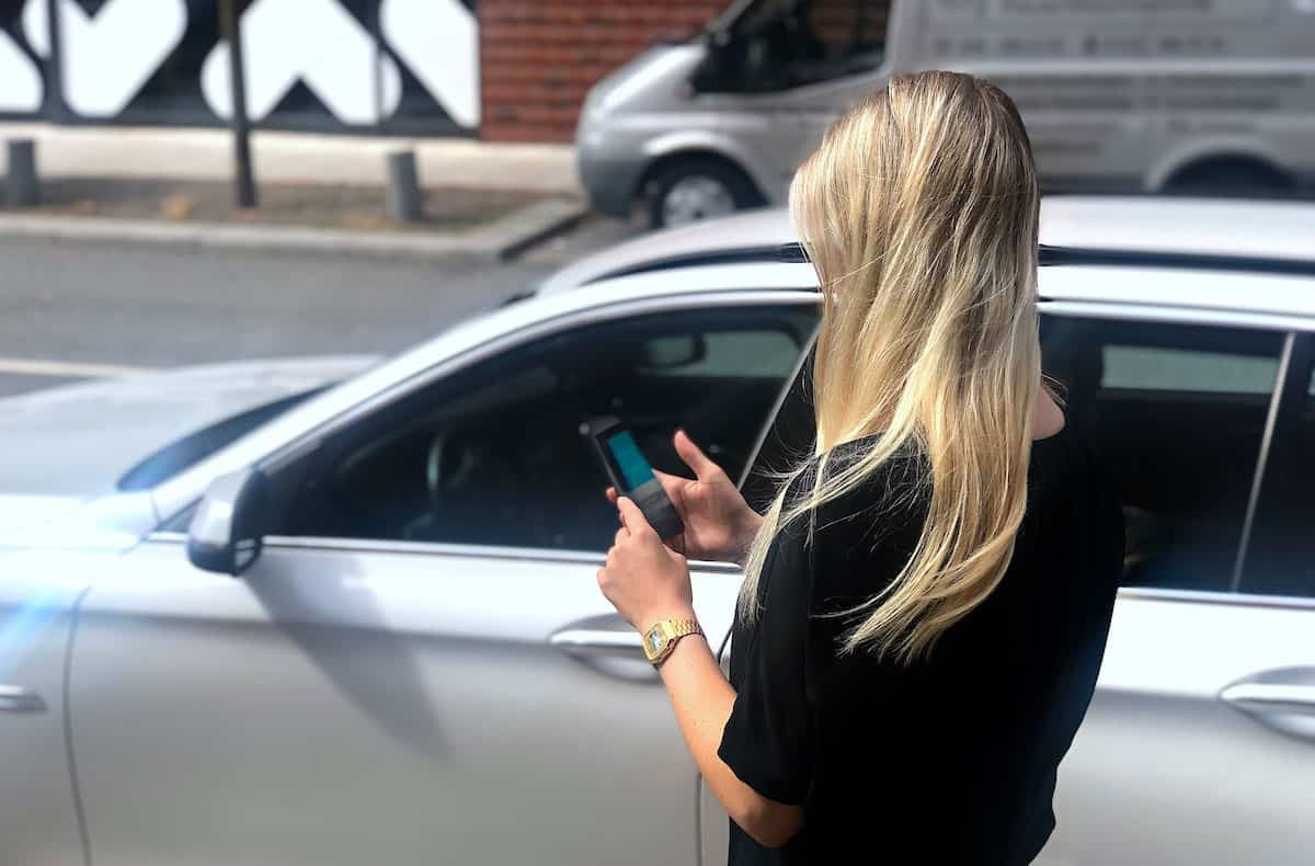 Caucasian female person looking at a mobile phone next to a silver car.