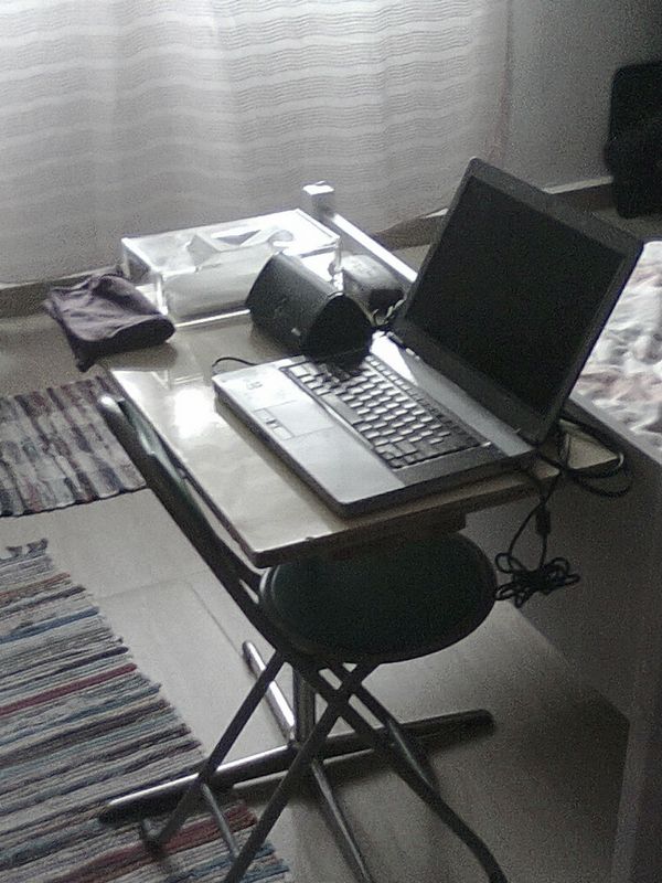 My desk in 2011: a very small table sitting at the bottom edge of my old bed, an old laptop with a broken speaker, and an external speaker sitting next to it. The chair was a foldable beach chair.