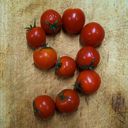 Ten cherry tomatoes forming the digit nine on a chopping board.