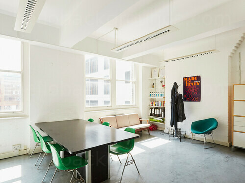 Light and simple meeting room decorated with white walls containing black table and metal framed green chairs  Microsoft Teams background