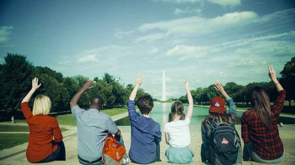 People seated in front of the Washington D.C. obelisk. They have one hand raised