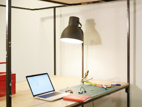 Simple creative office space with wooden desk featuring table top cutting matt and computer lit by adjustable lamp Microsoft Teams background