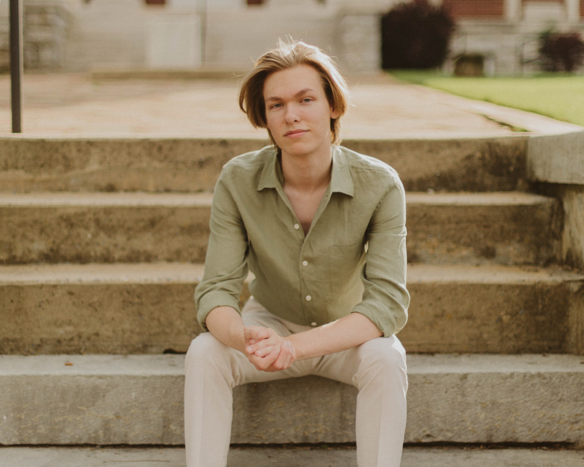 benton williams, photographer, in a green button-up shirt and white dress pants standing under a bridge with his camera in hand, looking into the distance.