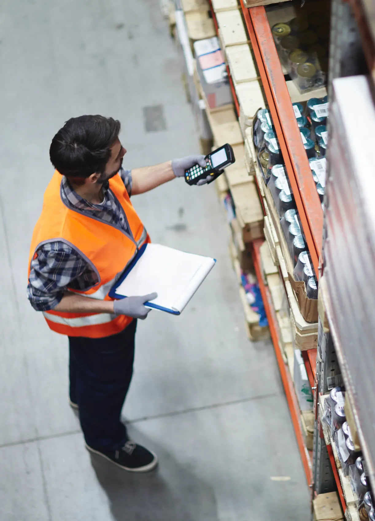 overhead view of man holding clipboard and scanning boxes in warehouse aisle