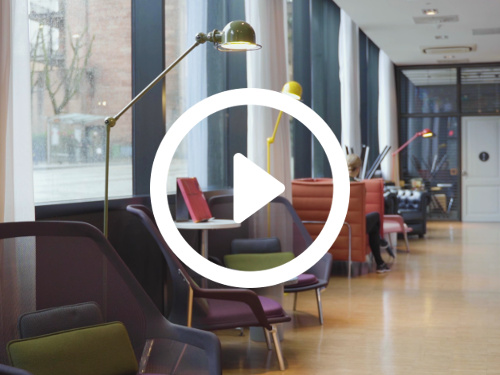 Modern shared workspace with assorted colourful seating next to adjustable reading lamps in front of large windows Skype background