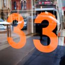 Street scene reflected in a window. Bright orange vinyl letters on the glass make the street number thirty three.