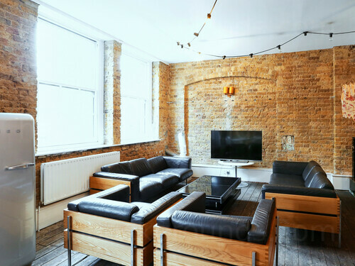 Light and airy meeting room with bare brick walls containing wooden framed leather upholstered sofas and chairs Microsoft Teams background