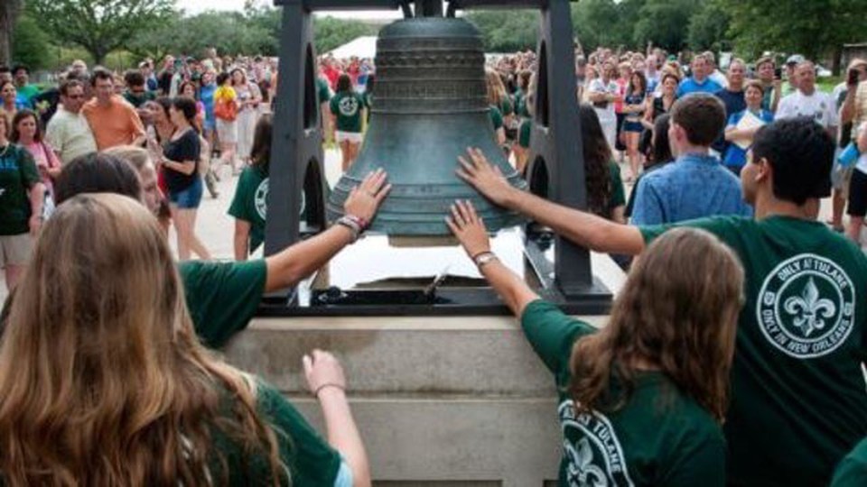 Students wearing a green Tulane University T-Shirt and touching a bell, while a lot of people watch