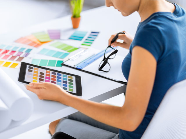 A Graphic Designer is reviewing color swatches both on an iPad, as well as on paper