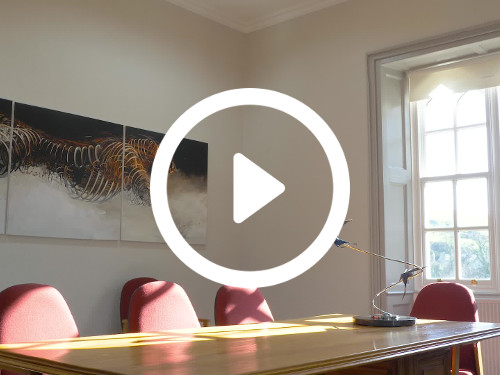 Contemporary naturally lit boardroom with wooden table and red padded chairs next to wall mounted art piece Microsoft Teams background
