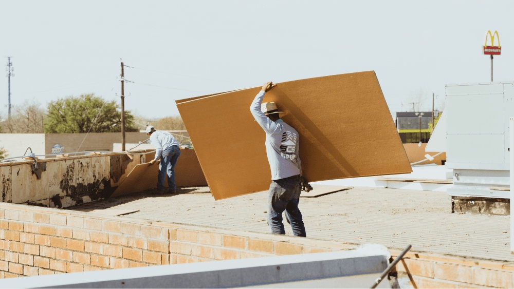 A worker carrying a large piece of plywood