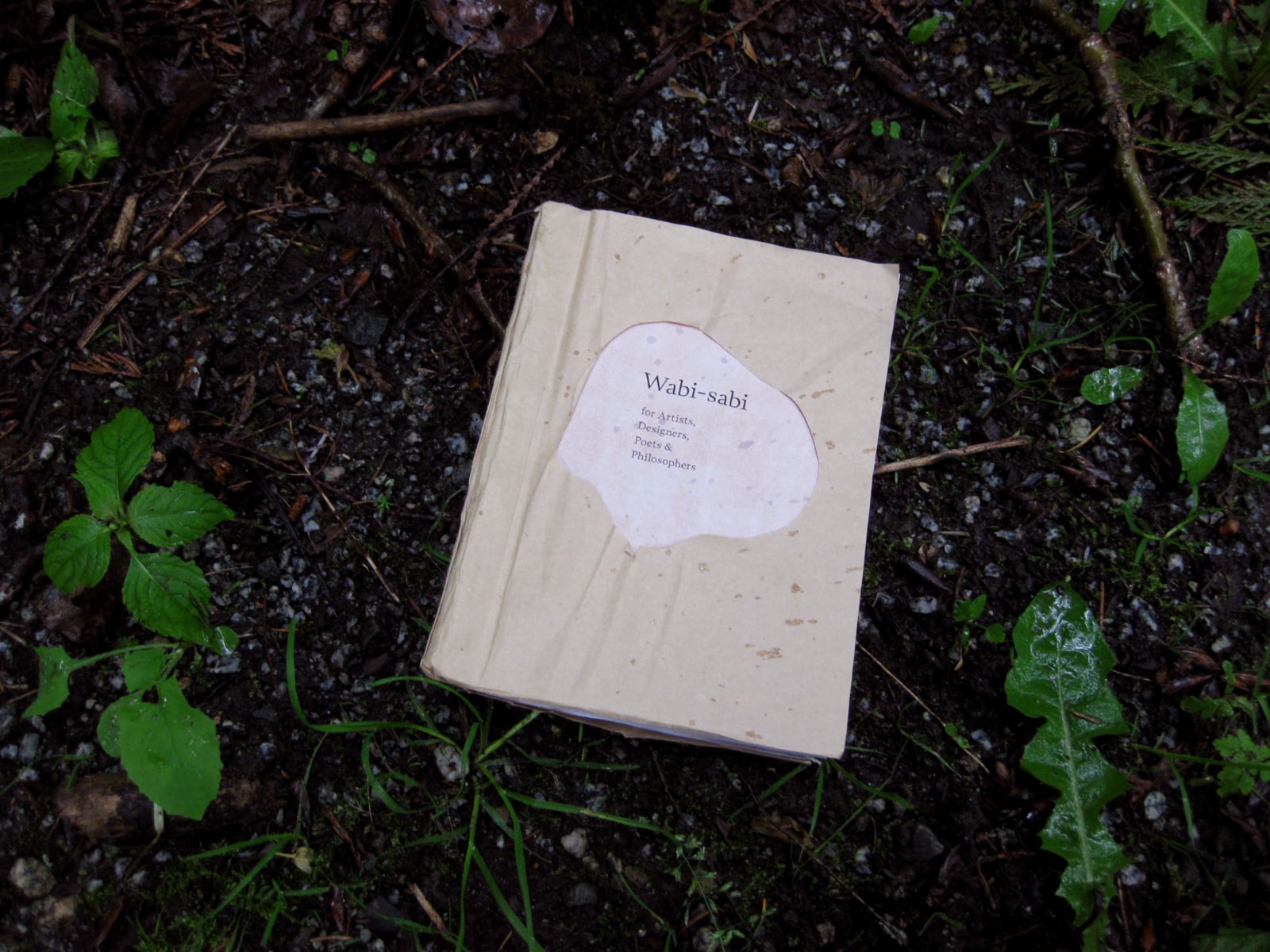 a book on a wet forest floor. Pages are closed. Title reads: Wabi-sabi for artists, designers, poets and philosophers.