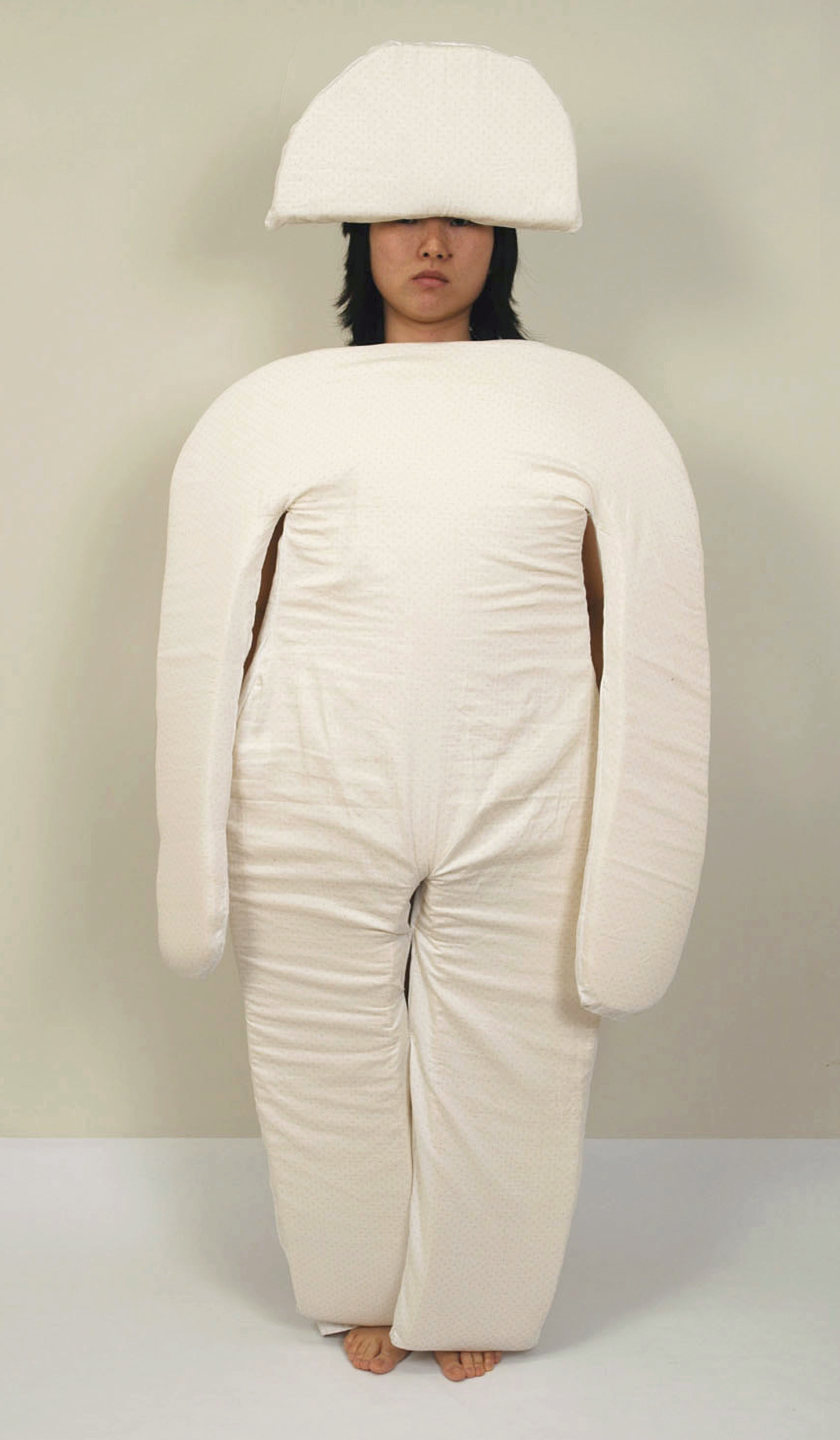 A woman wears the padding that would rest in the vertical bed: a series of cushions like an oversized set of pajamas, made to nest into the grooves and curves of the bed.