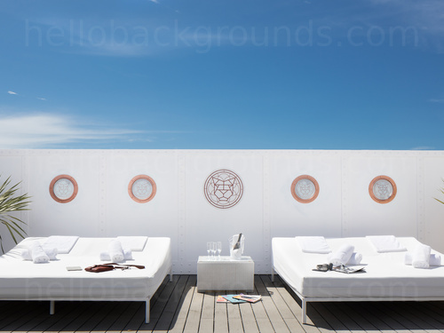 Luxurious outdoor deck with two sunbeds and drinks in a cooler, bright blue sky with a few wispy clouds Zoom background