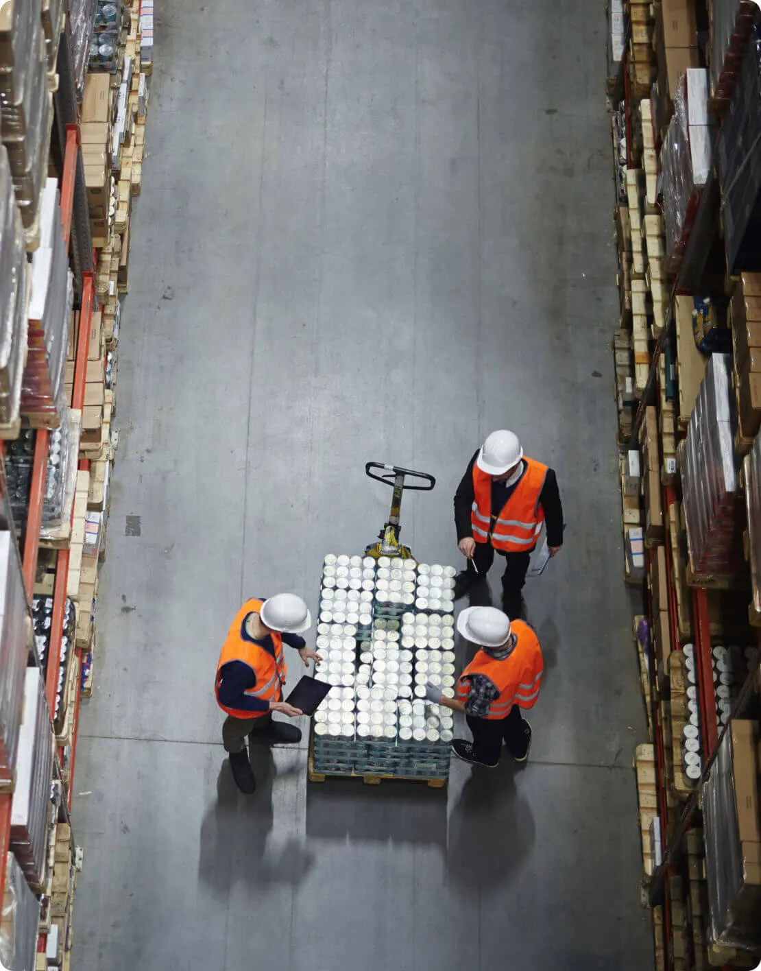 overhead view of three workers in safety vests and hard hats checking items on a moving cart in an aisle of a warehouse 2