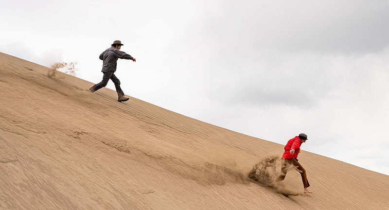Two men running down a sand dune at Christmas Valley Sand Dunes