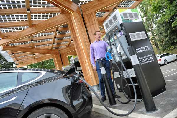 A man demonstrates K:Port in use by charging a Tesla electric car under the canopy