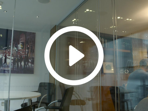 Intimate private office with glass walls containing white round table and black office chairs opposite wall mounted art Microsoft Teams background