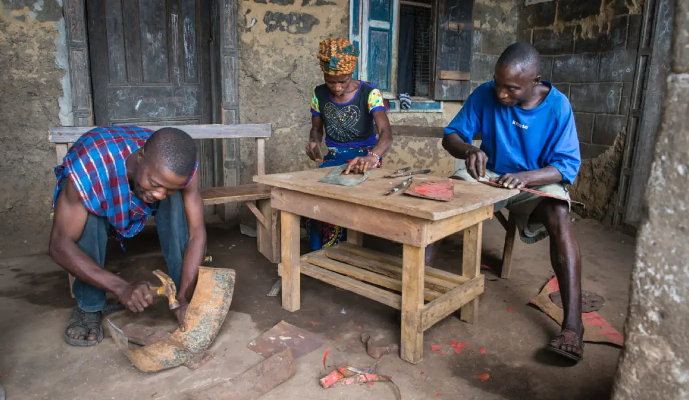 Three people work on scrap metal to make eco stoves.