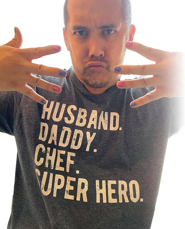 photo of Will sporting pink and blue nail polish, making a kissy face, while wearing a shirt that says husband, daddy, chef, super hero