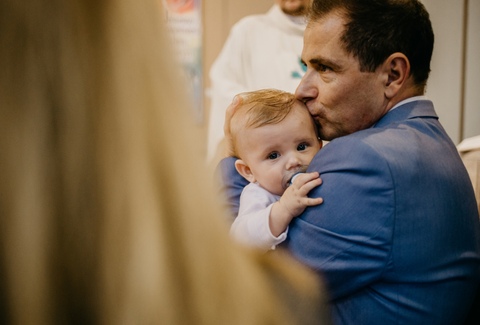 Zdjęcia chrztu Poznań - ojciec w garniturze trzymający dziecko do ceremonii