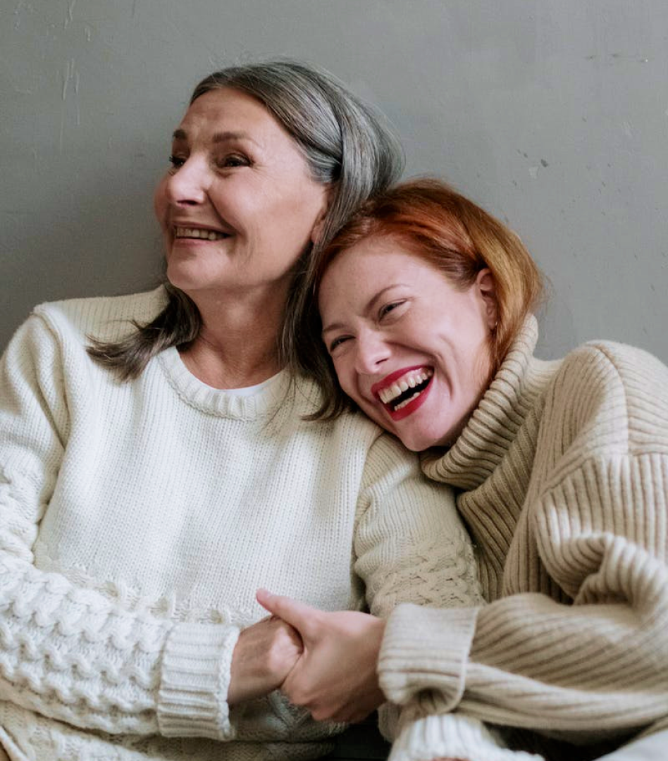 Young ginger woman and old gray-haired woman in thick sweaters laughing together