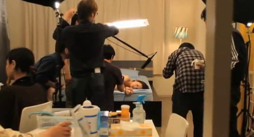 A screenshot showing behind-the-scenes of an adult film shoot. Film crew can be seen working on set and a table of snacks is in the foreground. From the film 'Nude'.
