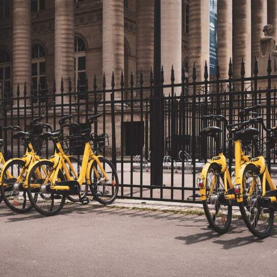 A row of yellow bikes parks on tall black railings outside an old building with pillars