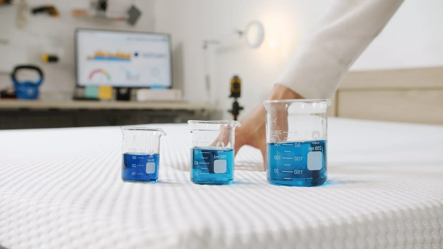 Three beakers filled with blue liquid on the top of a bed