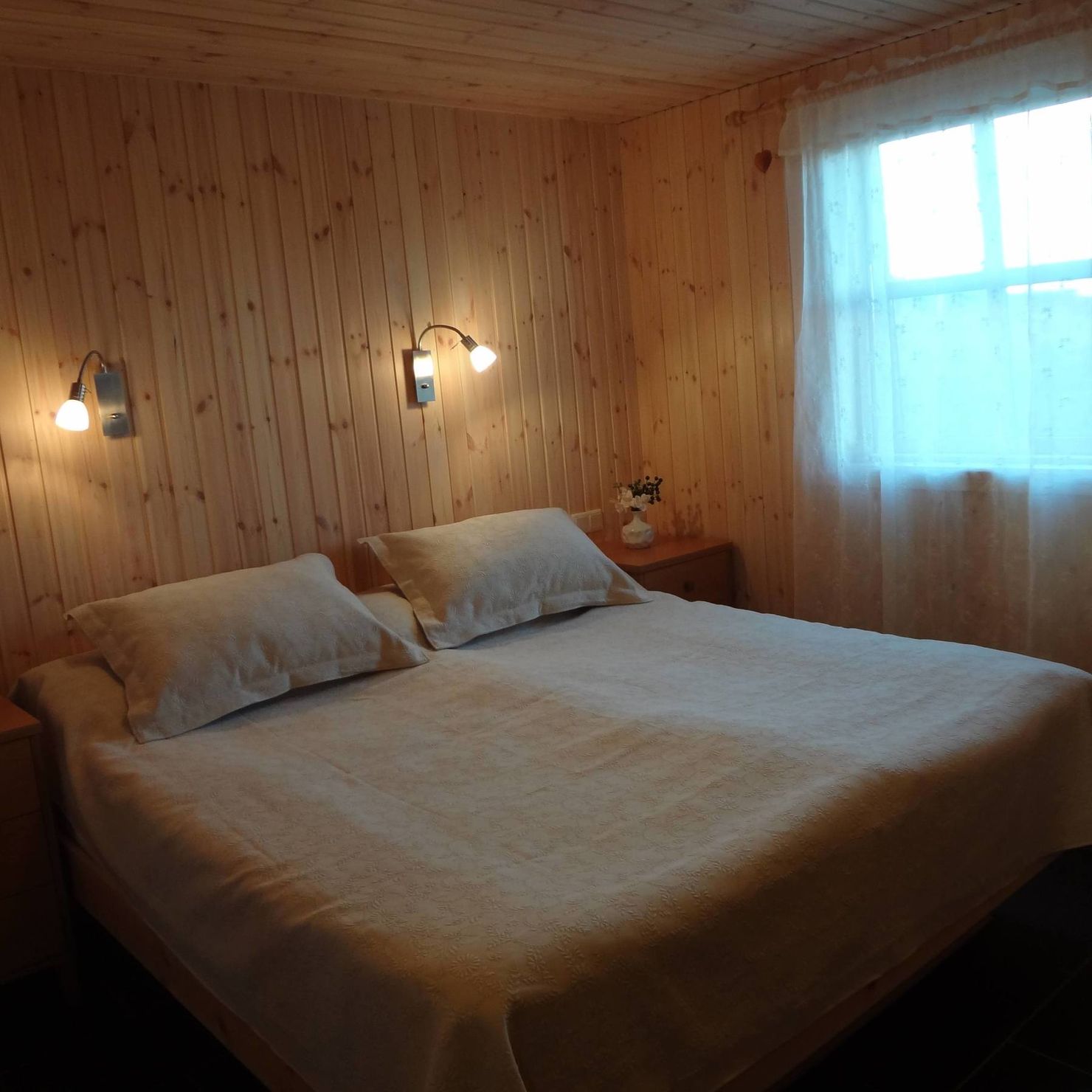 Ein großes Schlafzimmer mit Fenster, Leselampen und gemütlichem Doppelbett