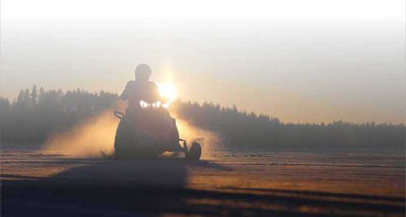 Snowmobiler riding at sunset Snowmobiler riding at sunset
