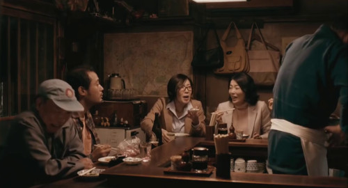 A screenshot of several patrons sitting at a Japanese pub counter sharing a lively conversation. From the movie 'Midnight Diner'.