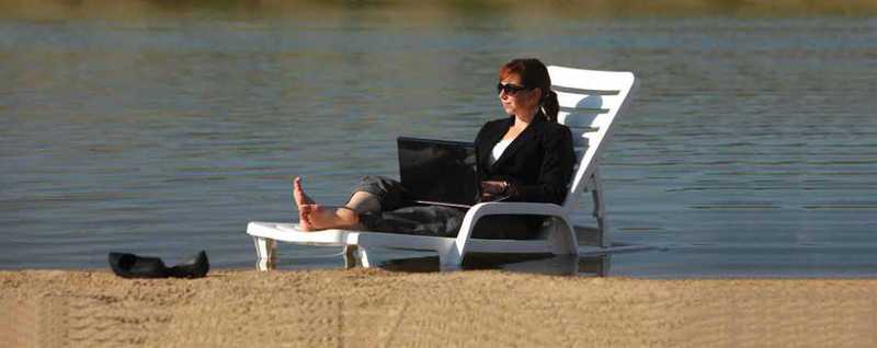 Woman on a lawn chair working on her laptop on a beach