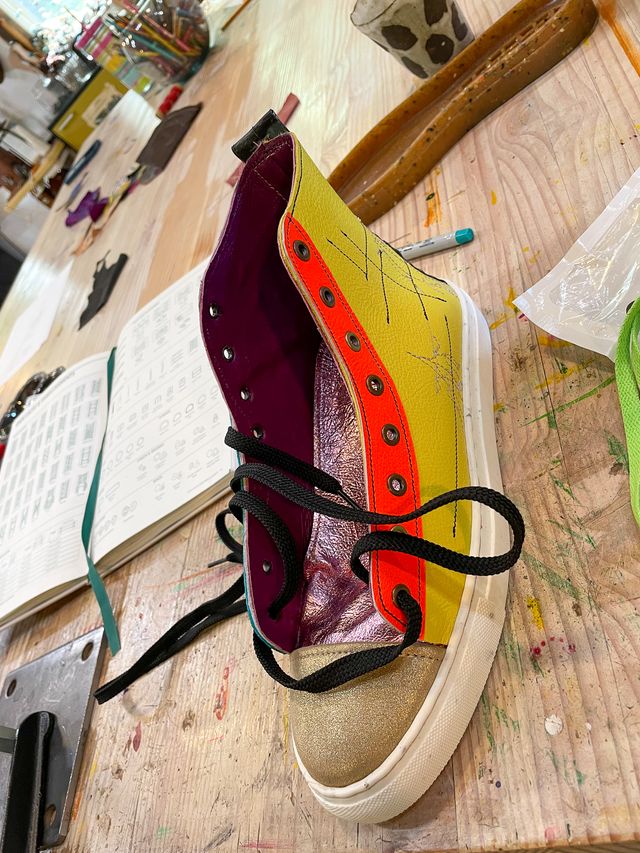 Shoe with a yellow & orange side
half-laced on the table
next to an open book of lacing varieties.
