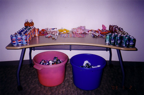The sugar table at the first Animarathon. Soda pops adorn the sides with snacks in the center of the table. Two buckets of additional soda are under the table.