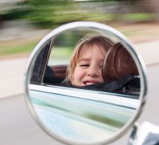 Mirror image of kid looking out car window with blurry background.