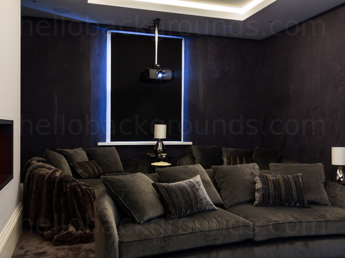 Dark screening room with blind drawn over window featuring a ceiling mounted projector and 2 large grey sofas Skype background